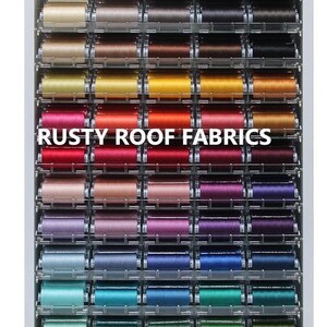 May include: A display of 60 spools of Efina 1500yd (1370m) thread in solid colors. The spools are arranged in a grid on a white shelf with the words "Rusty Roof Fabrics" printed in black.