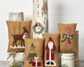Könnte beinhalten: Set mit vier festlichen Urlaubskissen. Jedes Kissen hat ein anderes Applikationsdesign: ein Rentier, einen Weihnachtsbaum, den Weihnachtsmann und eine Zuckerstange. Die Größen variieren von 11,4 cm bis 22,9 cm.
