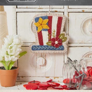 May include: A felt Uncle Sam hat decoration, 3" x 6.5", with red and white stripes, a blue brim and star, and floral accents. The design includes the text "UNCLE SAM HAT" and the brand name "BUTTERMILK BASIN DESIGN CO."