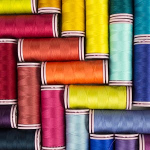 May include: A collection of spools of thread in various colors, including red, orange, yellow, green, blue, and purple. The spools are arranged in a grid pattern.