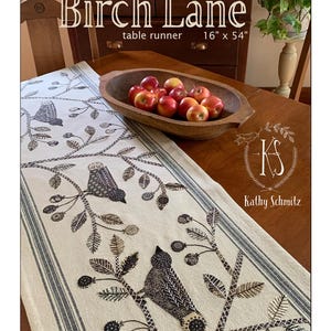 May include: A cream-colored table runner with a bird and branch design, measuring 16" x 54". The runner features a repeating pattern of birds perched on branches with leaves and flowers. The text "Birch Lane" is at the top.