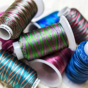 May include: A collection of spools of colorful embroidery thread. The thread is iridescent and has a variety of colors, including green, purple, blue, and red.