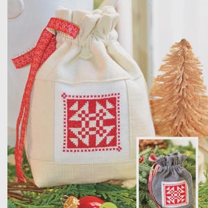 May include: A cream-colored drawstring bag with a red and white cross-stitch design. The bag has a red ribbon and the text "Christmas Piazza Cross Stitch". A small, similar bag is shown in the lower right corner.