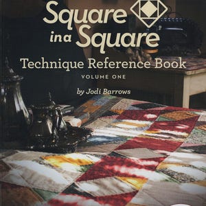 May include: A book cover titled "Square in a Square Technique Reference Book, Volume One" by Jodi Barrows. The cover features the title in large white letters, with a geometric design. The book is for quilters and promises to produce complex patterns with accuracy and ease.