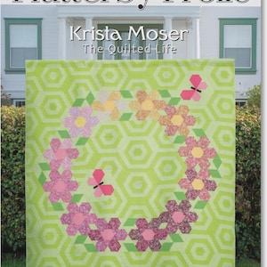 May include: A quilt pattern titled Flutterby Frolic by Krista Moser The Quilted Life featuring a light green hexagonal background with a floral wreath design in pink, orange, and yellow tones, plus two pink butterflies. Sizes: 76" x 84", 48" x 56", 12.5" x 41".