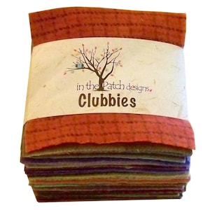May include: A stack of colorful fabric squares wrapped in a band of orange-red material. The wrapping features the text "in the Patch designs. Clubbies" with a tree logo. The fabric squares are various colors, including purple, green, and orange.