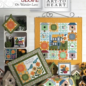 May include: A display of handmade quilts and decorative items with a sunflower theme. The quilts feature vibrant colors and intricate patterns, including sunflowers, birdhouses, and the text "You are my sunshine." The items are arranged on a wooden surface.