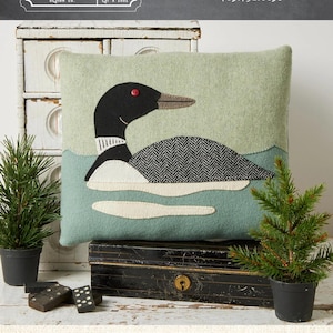 May include: A rectangular pillow featuring a loon design. The pillow has a light green background with a loon applique in black, white, and gray. The pillow measures 11 inches by 13 inches.