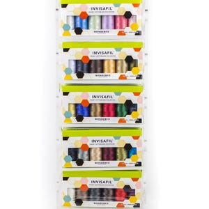 May include: A display of INVISAFIL applique thread packs. Each pack contains multiple spools of colorful thread. The packaging features the brand name, product details, and a geometric design with various colors.