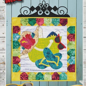 May include: A fabric wall hanging with a beach theme. The design includes a beach bag, sunglasses, and flip-flops. The text "BEACH DAY" is displayed above the image, with dimensions of 16.5" x 16.5".