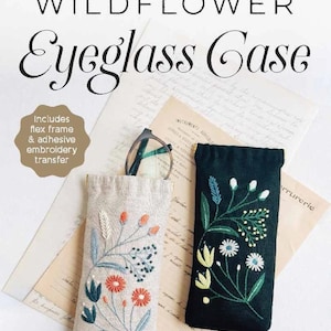 May include: Two eyeglass cases with floral embroidery. One case is beige with orange and blue flowers, the other is black with white and yellow flowers. The text on the image says "WILDFLOWER Eyeglass Case".