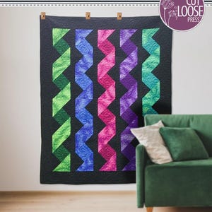 May include: A quilt titled Cascading Ribbons designed by Cathey Laird, featuring five vertical zigzag columns in green, blue, pink, and purple against a black background. The quilt measures 68.25 inches by 85 inches and uses a 10.5 inch square ruler.