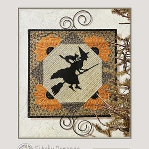 May include: A square quilt with a black witch silhouette on a broomstick, surrounded by orange and brown floral patterns. The quilt is 18 x 18 inches and features the text "Witchy Romance". Decorative metal scrollwork frames the quilt, with sprigs of greenery in the background.