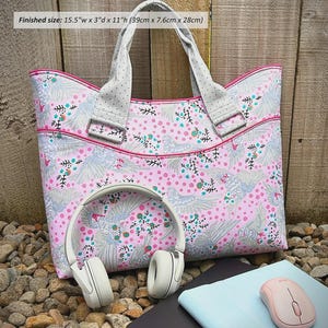 May include: A pink laptop bag with a bird and floral pattern, featuring grey polka-dot handles and pink piping. The bag measures 15.5 inches wide by 3 inches deep by 11 inches high. It is displayed with white headphones and a light blue mouse.