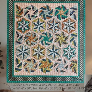 May include: A colorful quilt with a geometric starburst pattern. The quilt features a teal border with a black and white dotted trim. The central design includes various fabrics in shades of teal, orange, and cream. The quilt is labeled "Midnight Hex" and is a quilt pattern by Jennifer Wagner.