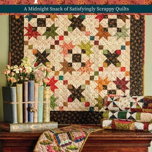 May include: A still-life arrangement featuring a quilt, books, and flowers. The quilt, titled "Simple Whatnots IV," has a star pattern in various colors. Books are tied with twine, and a small quilt rests on a wooden surface. The background is a floral pattern.