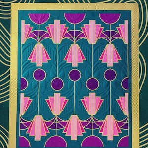 May include: A teal and gold quilt pattern with a geometric design. The quilt features pink and purple stylized floral shapes. The finished throw size is 57 1/4" x 69". The text on the quilt reads "LUNAR LUXE" and "QUILT PATTERN BY JENNIFER WAGNER".