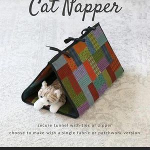 May include: A patchwork cat tunnel with a stuffed cat inside. The tunnel is made of various colorful fabric squares and has black ties at the top. The text "Cat Napper" is displayed above the tunnel.