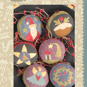 May include: Six felt Christmas ornaments with various designs, including a star, a house, a wreath, a Santa, a pudding, and an angel. The ornaments are arranged on a dark background with red berries and greenery.