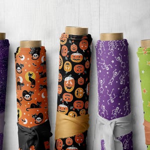 May include: Five rolls of fabric with different Halloween-themed patterns. The patterns include a purple fabric with white spiderwebs, an orange fabric with black cats and moons, a black fabric with orange pumpkins, a purple fabric with white skeletons, and a green fabric with white stars.