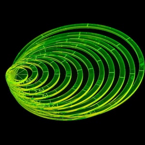 May include: A collection of neon green, semi-transparent, concentric circles against a black background. Each ring has markings and is slightly offset, creating a spiral effect. The image is well-lit, highlighting the vibrant color and geometric design.
