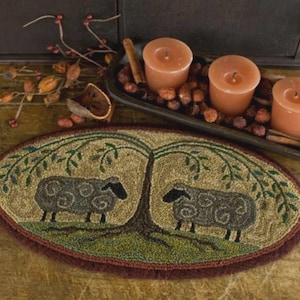 May include: Oval rug featuring two sheep under a tree. The rug has a green and brown color scheme with a dark red border. Three orange candles sit in a wooden tray with cinnamon sticks and nuts.