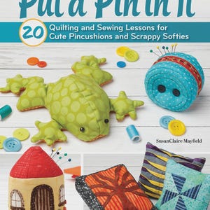 May include: A book cover titled Put a Pin in It: 20 Quilting and Sewing Lessons for Cute Pincushions and Scrappy Softies by SusanClaire Mayfield. The cover displays a green fabric frog, a blue pincushion, a house, and various quilted pillows.