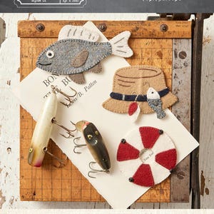 May include: A collection of three fishing-themed ornaments. Includes a felt fish, a hat with a fish charm, and a red and white life preserver. The ornaments measure approximately 3" x 4", 2.5" x 5", and 3" x 3".