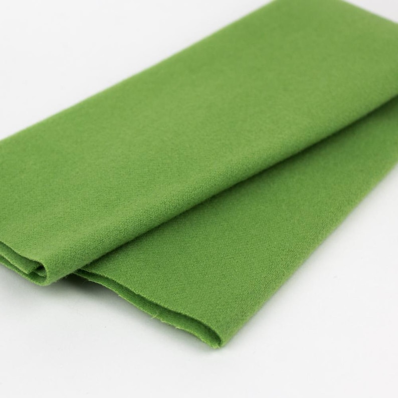 Puede incluir: Un trozo de tela de fieltro verde doblado. La tela es suave y tiene una textura ligeramente peluda.