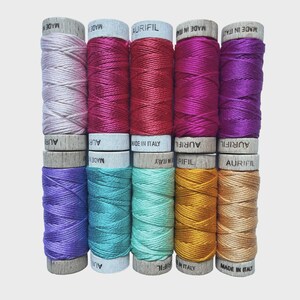 May include: A collection of Aurifil thread spools in various colors, including pink, red, purple, teal, gold, and tan. The spools are arranged in neat rows, with the brand name and "MADE IN ITALY" visible on the labels.