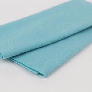 Puede incluir: Un trozo de tela de fieltro azul claro doblado. La tela es lisa y tiene una textura suave.