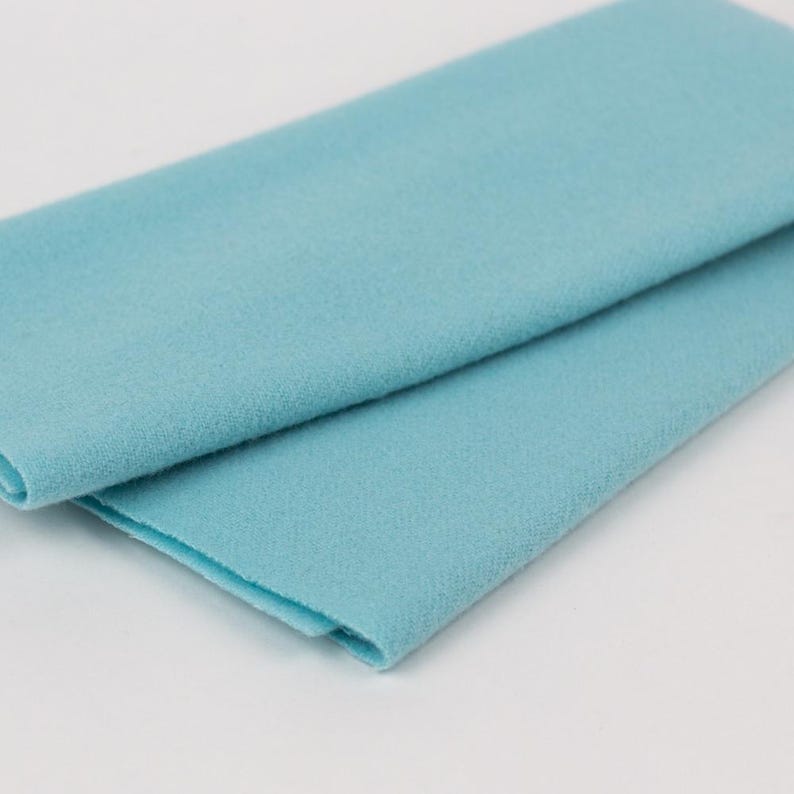 Puede incluir: Un trozo de tela de fieltro azul claro doblado. La tela es lisa y tiene una textura suave.