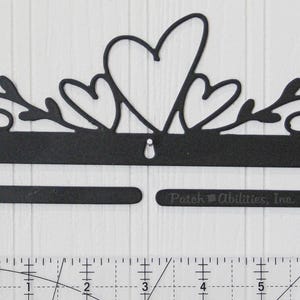 May include: Black metal wall decor featuring a heart and floral design. The decor has a horizontal bar with two openings and the text "Patch Abilities, Inc." The design includes a large heart and smaller hearts.