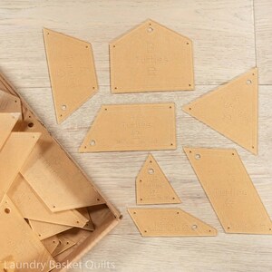 May include: A collection of tan acrylic quilt templates in various geometric shapes, including triangles, rectangles, and a house shape. Each template is labeled with letters and the word "Turtles". Some templates have pre-drilled holes.