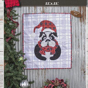 May include: A square quilt featuring a bulldog wearing a Santa hat and scarf, with the text "CUTEST BRUTUS" above. The quilt measures 22" x 25" and has an easy skill level. The design incorporates red and black plaid patterns.