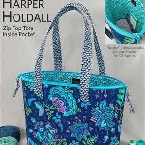 May include: A blue tote bag with a floral pattern, featuring a zip top and inside pocket. The bag has handles with a scale-like design. The text "Lazy Girl Designs" and "HARPER HOLDALL" are visible. Size is 13" x 13" x 6".