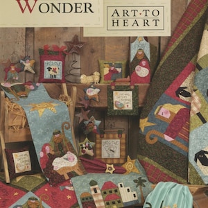May include: A collection of Christmas-themed fabric crafts, including quilts, pillows, and table runners. The items feature nativity scenes, stars, and the text "Star of Wonder", "Art to Heart", "Bless Ewe", and "Adore". The color palette includes red, green, and blue.