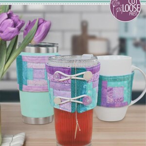 May include: A pattern instruction sheet titled Log Cabin Cozies by Cut Loose Press. The image displays three beverage containers wrapped in quilted fabric sleeves featuring purple and teal patchwork designs, secured with white elastic and buttons.
