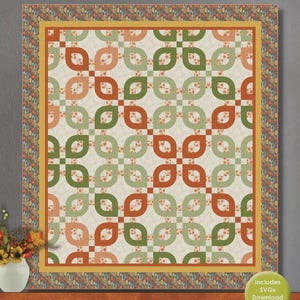 May include: A quilt with a repeating pattern of green and orange leaf-like shapes on a cream background. The quilt has a yellow border and a patterned edge. The word "Autumn" is printed at the bottom. A small vase of flowers is in the corner.