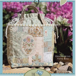 May include: A quilted fabric drawstring tote bag titled Tully Tote, featuring a patchwork design with floral and geometric patterns in muted green, pink, and tan tones. The bag includes an embroidered oval floral motif and two fabric handles.