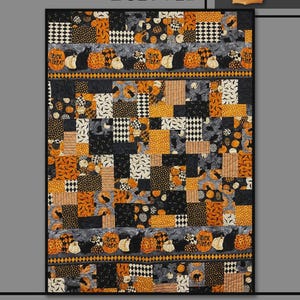 May include: A rectangular quilt featuring a patchwork design of black, orange, and white fabrics with patterns of pumpkins, black cats, and checkered squares. The quilt includes horizontal border strips with the text Trick or Treat.