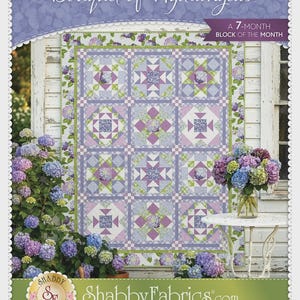 May include: A quilt pattern titled "Bouquet of Hydrangeas" with a floral design in shades of purple, green, and white. The quilt is displayed outdoors with a backdrop of hydrangeas and a white table. The text "A 7-MONTH BLOCK OF THE MONTH" is also visible.