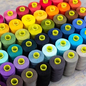 May include: A collection of spools of colorful thread, arranged in a rainbow pattern. The spools are all the same size and shape, and they are all wound with thread. The thread is a variety of colors, including red, orange, yellow, green, blue, indigo, and violet.