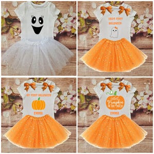May include: Four white and orange Halloween tutu outfits for babies. The outfits feature a white short-sleeved shirt with a Halloween-themed design and an orange tulle skirt with glitter. The designs include a ghost, a pumpkin, and the text "My First Halloween" and "Cutest Pumpkin in the Patch".