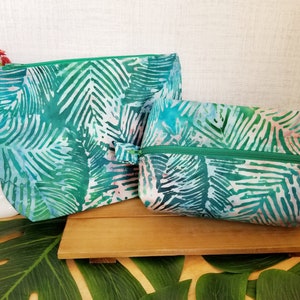 May include: Two green and white patterned zippered pouches with a leafy design. The pouches are made of fabric and have a green zipper.