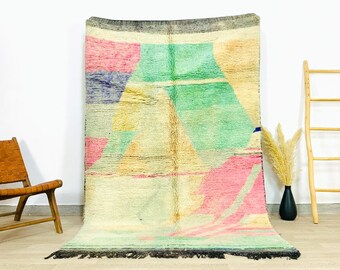 May include: A colourful abstract rug with geometric shapes in shades of pink, green, yellow, and blue. The rug has a fringe border and is made of wool.