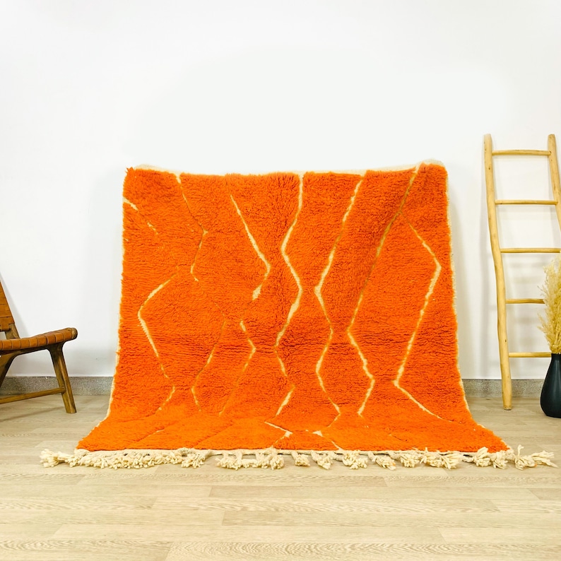 Puede incluir: Una alfombra marroqu&iacute; grande, de color naranja y crema, con un patr&oacute;n geom&eacute;trico. La alfombra tiene un borde de flecos y est&aacute; hecha de lana.