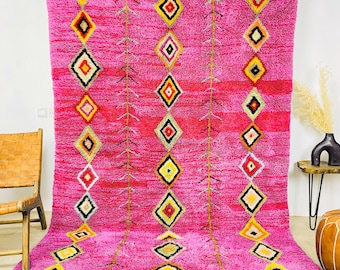 May include: A pink Moroccan rug with a geometric diamond pattern in shades of yellow, black, and white. The rug has a fringe border.