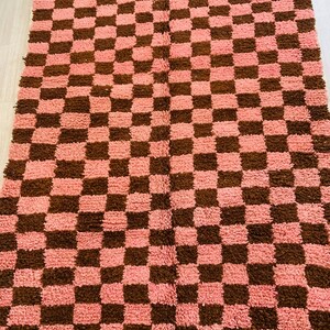 May include: A pink and brown checkered rug with a fluffy texture.