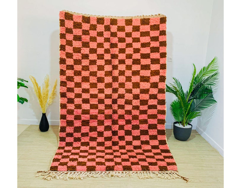 May include: A pink and brown checkered rug with a fringe border. The rug is made of a soft, fluffy material and has a vintage look.